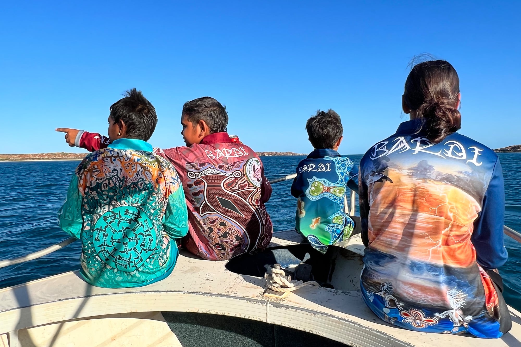 Bardi kids sitting on the front of a dingy wearing Ardi'ol designed fishing shirts
